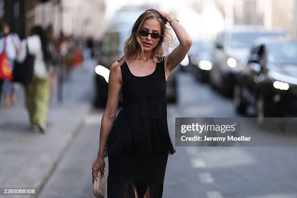 Ginta is seen wearing a black sleeveless fringe dress by Alaïa with a scoop neckline, a fitted bodice, a layered fringed skirt and a midi length hem,...