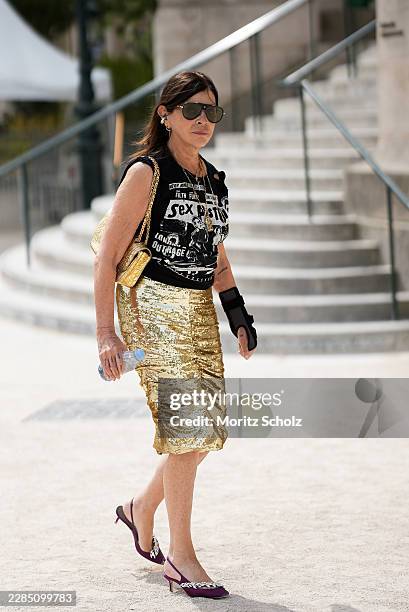 Carine Roitfeld is seen wearing a black sleeveless Sex Pistols graphic top; gold chain necklaces; a gold sequin pencil skirt with front slit from...