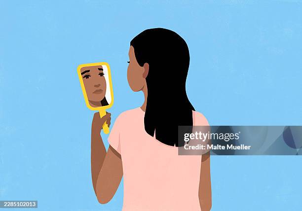 sad, crying woman looking at reflection in handheld mirror against blue background - low self esteem stock illustrations
