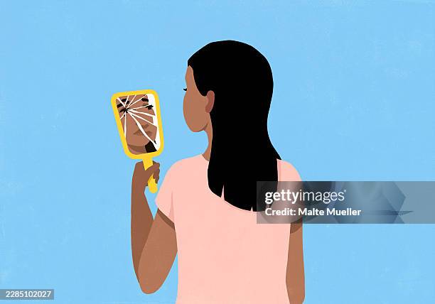 young woman looking at reflection of her face in cracked vanity mirror against blue background - low self esteem stock illustrations