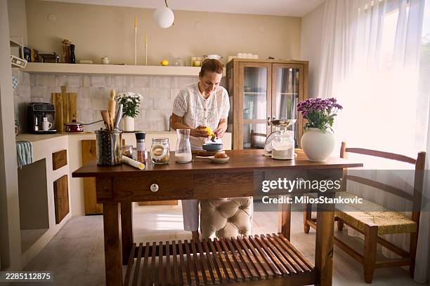 woman zesting lemon while baking in bright home kitchen with rustic wooden island - kitchen island stock pictures, royalty-free photos & images