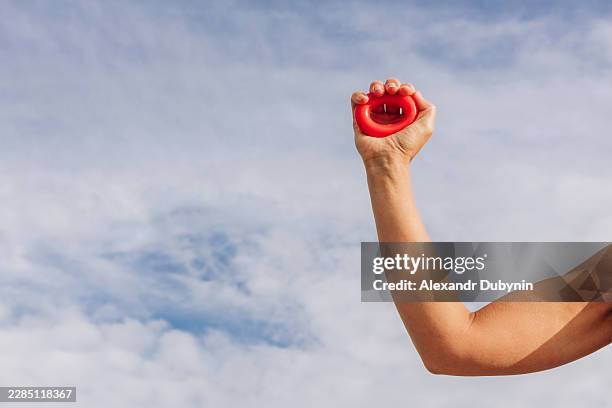 female strong arm with expander outdoors against sky background - wrist stock pictures, royalty-free photos & images