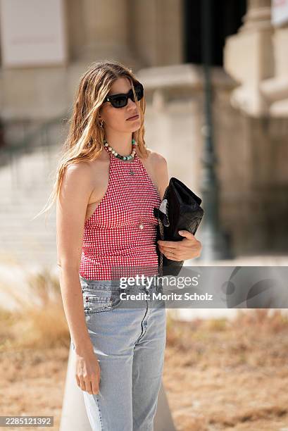 Veronika Heilbrunner is seen wearing a red and white gingham sleeveless halter neck top; light blue straight leg denim jeans; a medium sized black...