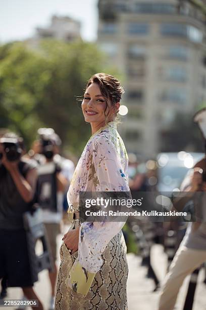Olivia Palermo wears a sheer floral blouse tucked into a beige snakeskin-print pencil skirt, gold hoop earrings, carries a pale yellow clutch,...