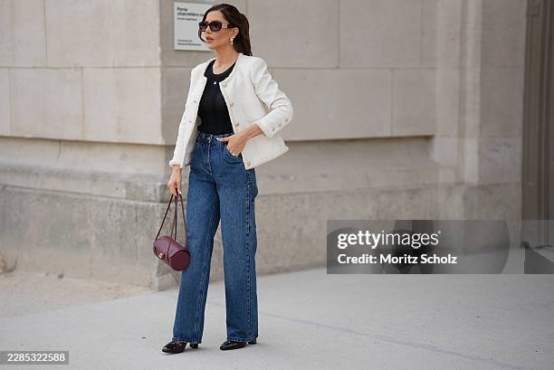 Guest is seen wearing a white textured cropped jacket from Chanel with button front and frayed trim; a black ribbed sleeveless top; blue wide leg...