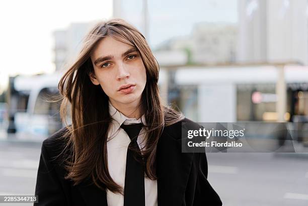 androgynous young man portrait in suit and tie with long hair on city street - staring stock pictures, royalty-free photos & images