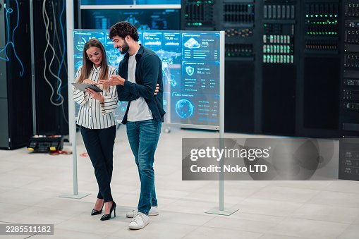 Engineers analyzing data on a tablet in a modern data center with server racks and interactive display Engineers analyzing data on a tablet in a modern data center with server racks and interactive display