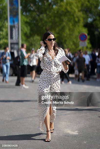 Guest is seen wearing a white long sleeve polka dot shirt dress with a knotted waist detail and front slit; black ankle strap sandals; black oval...