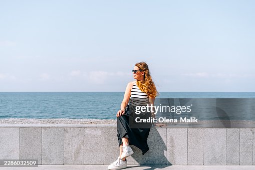 Woman Relaxing on Rocks Facing Sun by the Sea Woman Relaxing on Rocks Facing Sun by the Sea
