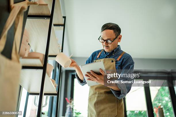 ceramic studio owner inspecting handmade pottery mug while updating inventory records on digital tablet - taking inventory stock pictures, royalty-free photos & images