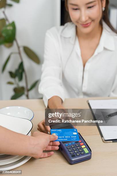small business owner processing orders, asian female entrepreneur accepts digital payment, customer taps card reader for online purchase, cashless checkout, pos keypad, invoice clipboard, desk. - contactless delivery stock pictures, royalty-free photos & images