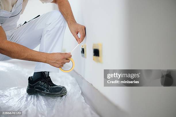 professional painter masking electrical outlets while preparing interior wall for painting in home - paint scraper stock pictures, royalty-free photos & images