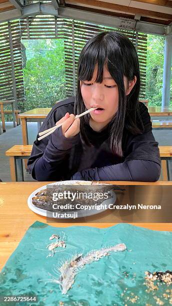 young girl eating grilled fish with chopsticks outdoors. with uv protection gloves - disposable bbq stock pictures, royalty-free photos & images