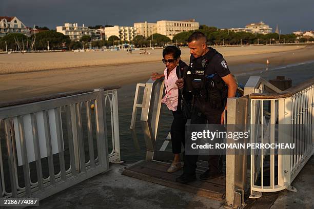 Police officer helps a holidaymaker from Lege-Cap-Ferret upon her arrival in Arcachon by boat during an evacuation operation of the entire Cap-Ferret...
