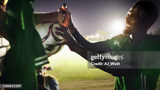 Young male football player signing autographs for fans after night match Young male football player signing autographs for fans after night match