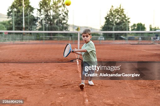 Junger Tennisspieler mit fokussiertem Ausdruck beim Ballschlag Junger Tennisspieler mit fokussiertem Ausdruck beim Ballschlag