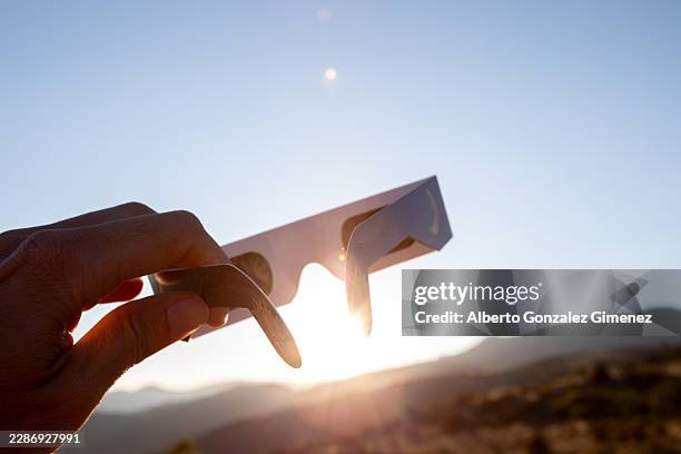 hand holding eclipse glasses watching solar event - eclipse people stock pictures, royalty-free photos & images