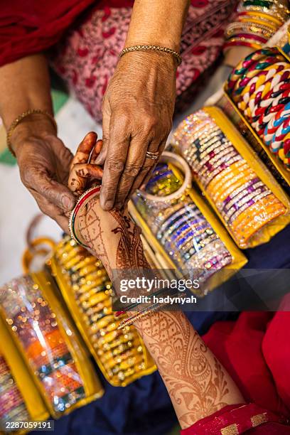 bangle fitting with henna-adorned arm — jaipur, india - bangle stock pictures, royalty-free photos & images