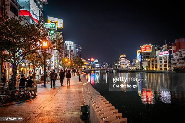 river in fukuoka with people walking in the street at night with highrise apartments offices mall and tarpaulin fukuoka japan - fukuoka prefecture stock pictures, royalty-free photos & images