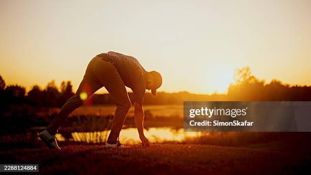 golfer placing ball on tee at sunset - golfer sunset stock pictures, royalty-free photos & images
