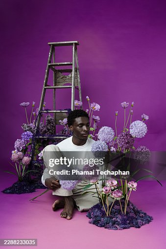 Thoughtful Man Sitting Among Purple Flowers in Botanical Environment Thoughtful Man Sitting Among Purple Flowers in Botanical Environment