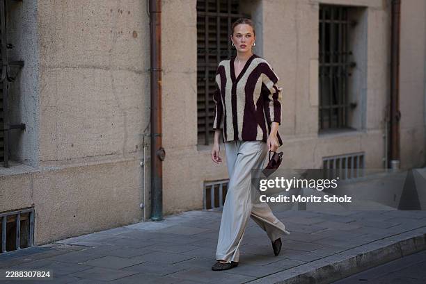 Pia Riegel is seen wearing a burgundy and cream striped oversized knit cardigan from H&M; cream wide leg trousers from mapa; black woven ballet flats...