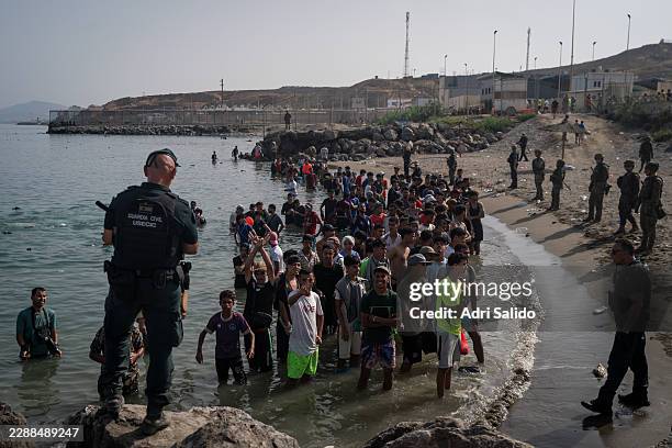 Members of the Guardia Civil USECIC guard migrants on Tarajal beach after crossing the border between Spain and Morocco on July 31, 2026 in Ceuta,...