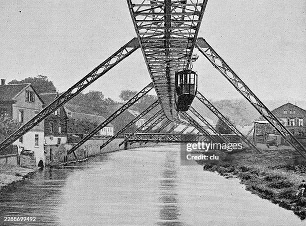 elberfeld suspended railway gliding above the river wupper — suspended carriage floats beneath the steel framework between riverside houses - monorail suspended stock illustrations