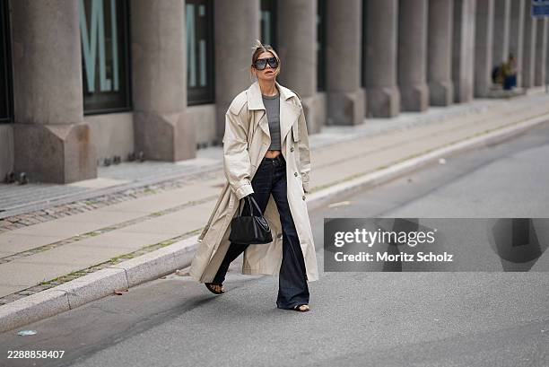 Sophia Geiss is seen wearing a beige oversized double breasted cotton trench coat with wide lapels, epaulettes, storm flap, adjustable cuff straps...