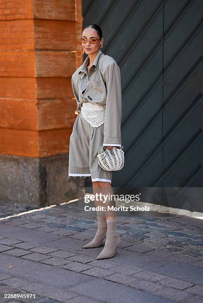 Guest is seen wearing an oversized taupe button up shirt with dropped shoulders; matching oversized knee length tailored shorts layered over white...