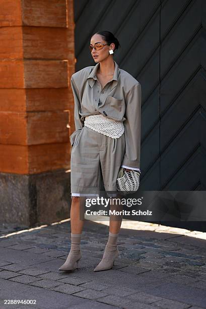 Guest is seen wearing an oversized taupe button up shirt with dropped shoulders; matching oversized knee length tailored shorts layered over white...