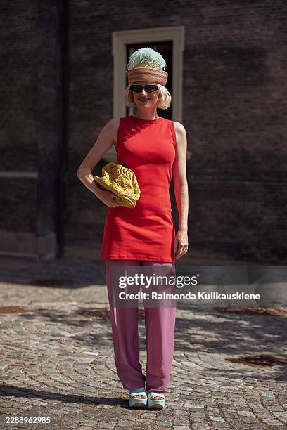 Pernille Rosenkilde wears black sunglasses, a striped hat topped with mint-green feathers, a red sleeveless tunic over pink straight-leg trousers,...