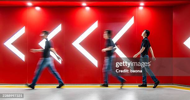 conceptual business, multiple exposure man walking along direction of the arrows in front of red wall - exposição longa imagens e fotografias de stock