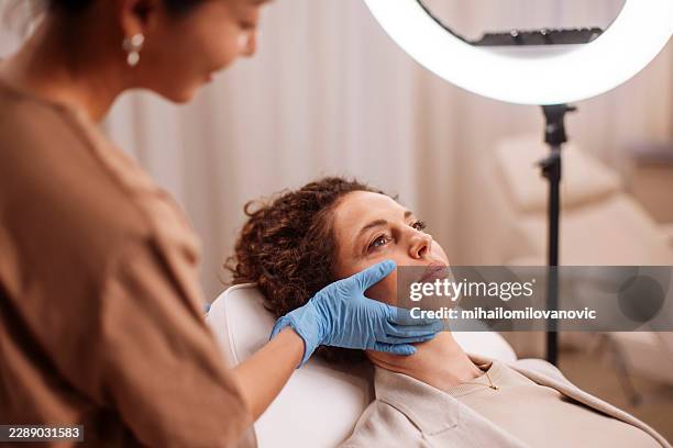 cosmetic consultation with dermatologist examining woman's face in clinic - surgical glove stock pictures, royalty-free photos & images