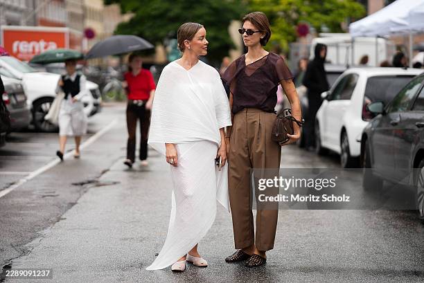 Tina Haase is seen wearing a white pleated draped cape top; a white pleated maxi skirt; white pointed toe slingback flats; pearl stud earrings; a...