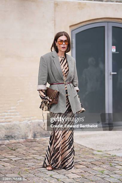 Guest wears shoulder-length straight brown hair with a center part, tortoiseshell aviator sunglasses with orange tinted lenses, a gray check blazer...