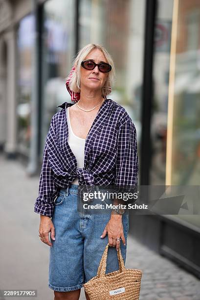 Guest is seen wearing a purple checked button-up shirt tied at the waist over a white tank top; light blue denim Bermuda shorts; oval sunglasses; a...