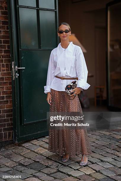 Cris Mata wears an oversized white shirt cinched with a slim belt, a sheer embellished maxi skirt and embellished heels while arriving at the...