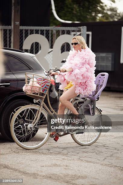 Pernille Rosenkilde on a bicycle wears yellow mini shorts, pink flower petal imitation jacket, red sandals and black Chanel sunglasses outside Stine...