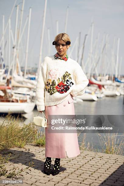 Guest wears pink maxi skirt, white sweater with flower ornaments, white bag, black shoes with a socks with polkadots and black hair accessory that...