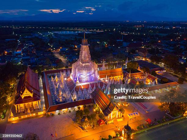 high angle aerial drone view of wat phra mahathat woramahawihan fully illuminated at twilight in nakhon si thammarat, southern thailand. stunning cityscape overview showing the main stupa under renovation surrounded by satellite pagodas and temple compoun - nakhon si thammarat stock pictures, royalty-free photos & images