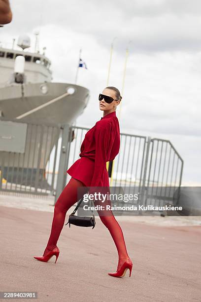 Indre Burlinskaite wears a monochrome red long sleeve blouse with matching red leggings, oversized black sunglasses, carries a black shoulder bag and...