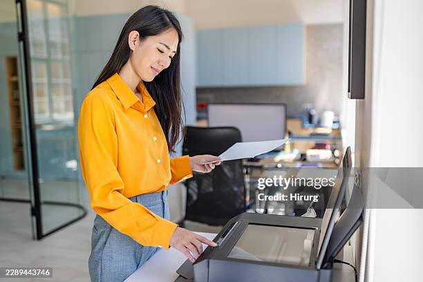 young woman using a printer in a modern office setting with bright lighting - computer documents stock pictures, royalty-free photos & images