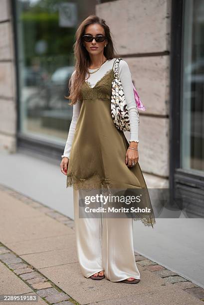 Evi Wave is seen wearing an olive green silk slip dress with lace trim and an asymmetric hem from Gestuz; a white long sleeve gathered top from Rich...
