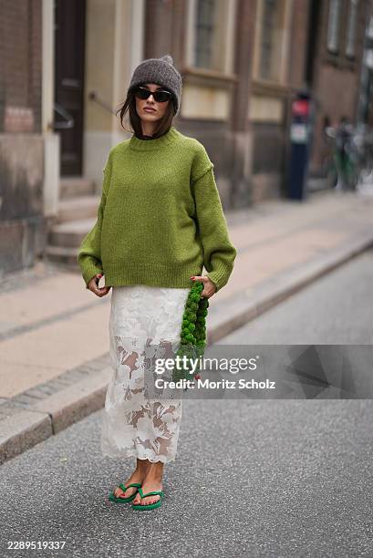 Evi Wave is seen wearing an oversized green knit sweater from Miyami; a white floral lace midi skirt from MALINA; green rubber flip flops from...