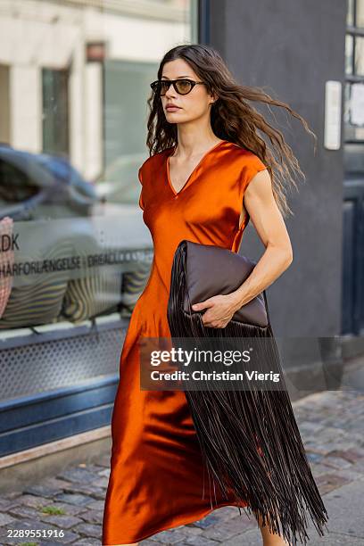 Guest wears rust brown shiny sleeveless v neck dress Marella, black fringed bag, Sportmax, sunglasses Prada during the Copenhagen Fashion Week...