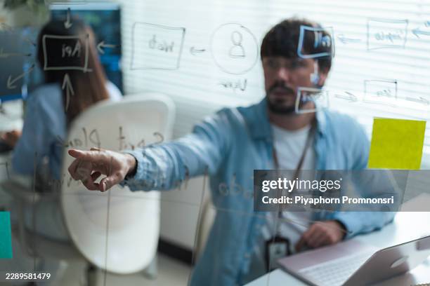 selective focus finger of software developer examining business workflow on transparent board in bright office. supporting project management and software development. - software development stock pictures, royalty-free photos & images