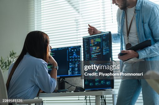 Female developer listens as colleague explains coding structure on multiple screens in office. supporting teamwork, software development, data science, debugging, security and cloud computing. Female developer listens as colleague explains coding structure on multiple screens in office. supporting teamwork, software development, data science, debugging, security and cloud computing.