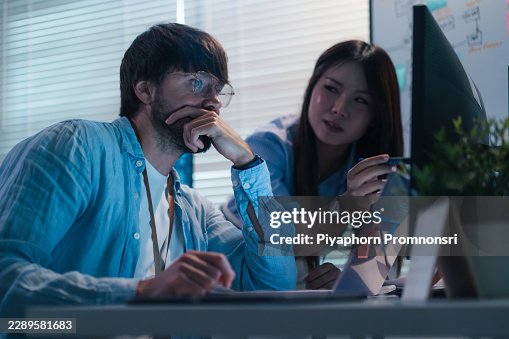 Female computer programmer explaining coding solution to colleague concentrates on computer monitor in modern office, discussing coding solution, debugging, software development, data and teamwork. Female computer programmer explaining coding solution to colleague concentrates on computer monitor in modern office, discussing coding solution, debugging, software development, data and teamwork.