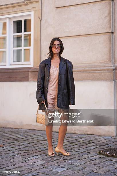 Guest wears shoulder-length straight brown hair with a center part, oversized square sunglasses with dark lenses, a black leather oversized blazer...